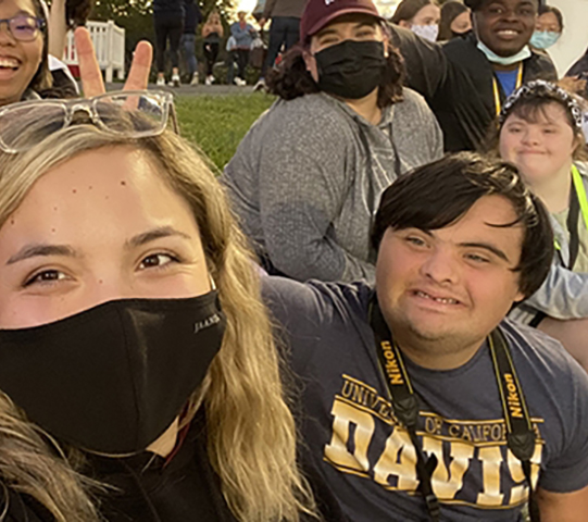 Group of smiling people outdoors, some wearing masks, enjoying a social gathering.