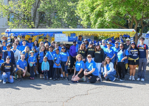 A group of volunteers and family members wearing matching Give Day shirts in front of the decorated parade tram on Picnic Day.