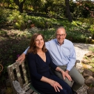 Renée and Mike Child seated on a park bench outside in a garden.